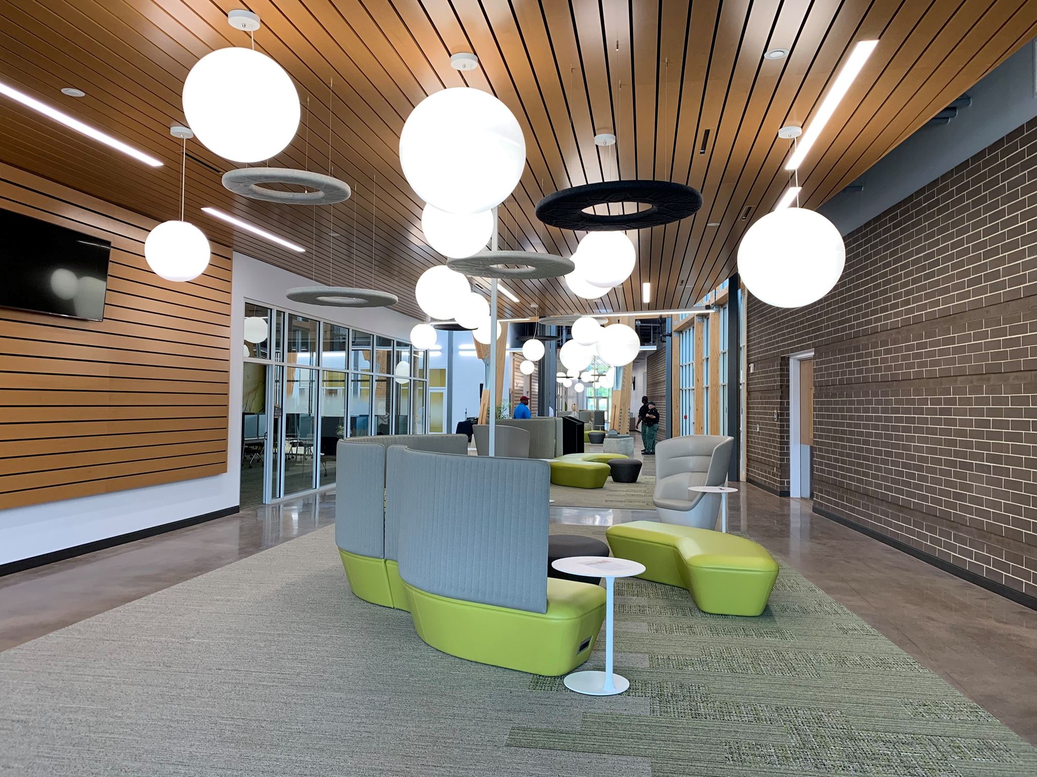 Interior of The Continuum lobby showing vibrant green and grey bench seats and globe lights hanging from a modern wood-slat ceiling